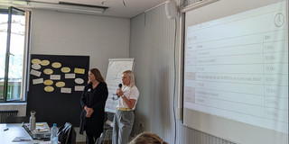 Auf dem Bild sind Yana York und Sarah Lamb zu sehen , die vorne in einem Raum eine Präsentation halten.